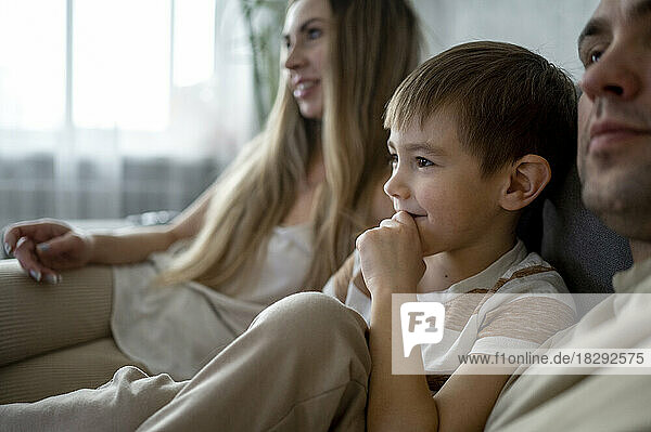 Lächelnder Sohn verbringt seine Freizeit mit den Eltern zu Hause auf dem Sofa