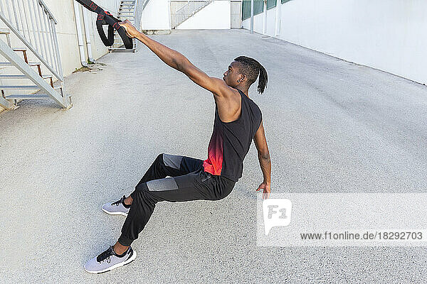 Young man practicing with suspension straps outdoors