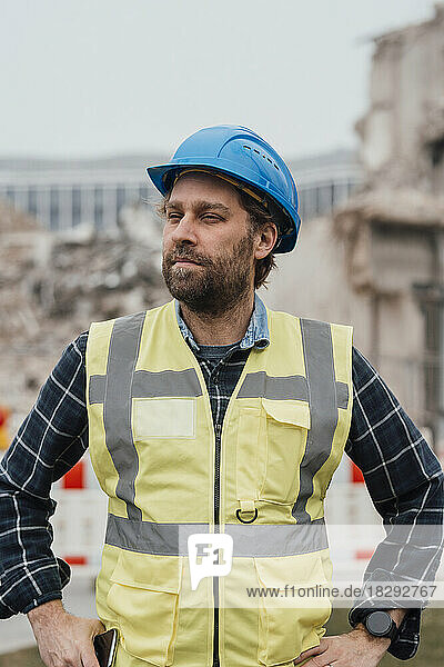 Mature worker wearing hardhat with hands on hips at construction site