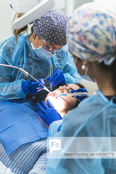 Dentist with assistant examining patient with tools and equipment in clinic