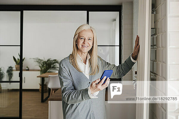 Happy mature woman standing with mobile phone at home