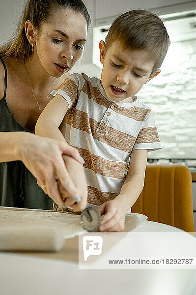 Mother and son cutting croissant dough on table in kitchen at home