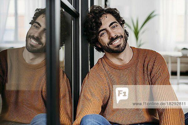 Happy young man leaning on glass door at home