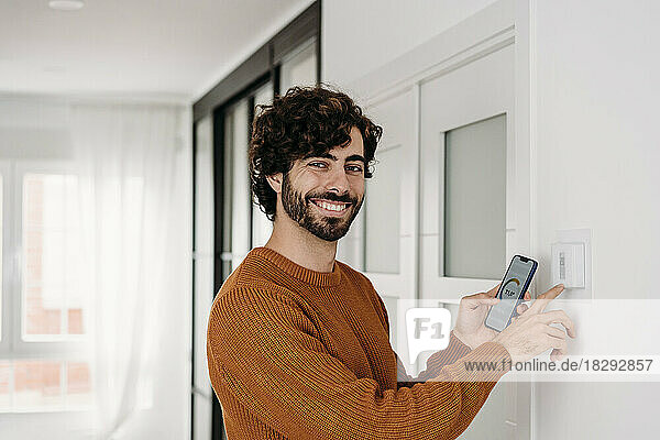 Happy young man operating thermostat with smart phone at home