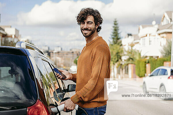 Happy man charging car at electric vehicle charging station