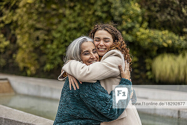 Happy young woman hugging grandmother in park