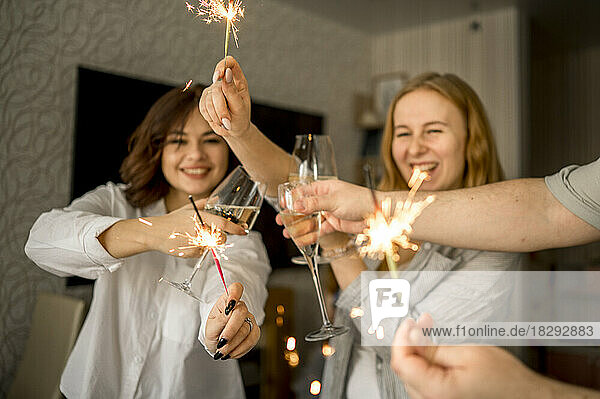 Cheerful friends celebrating with glasses of champagne and sparklers at home