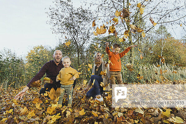 Happy parents with playful children throwing autumn leaves in forest