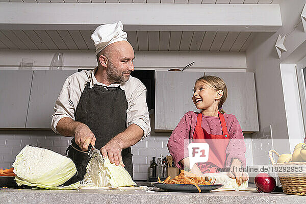 Father and daughter wearing aprons preparing healthy meal in kitchen at home