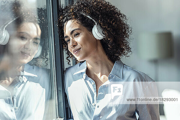 Contemplative smiling woman with headphones looking through window