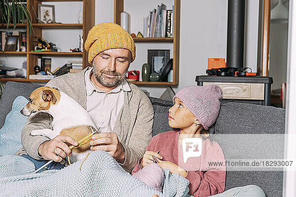 Vater und Tochter mit Hund stricken gemeinsam auf der Couch zu Hause