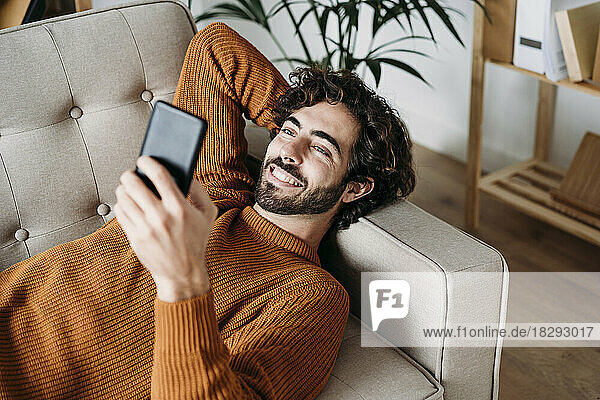 Happy young man using smart phone on sofa
