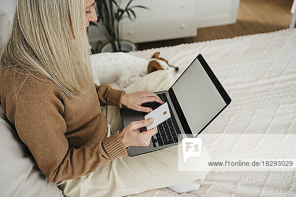 Mature woman paying with credit card through laptop in bedroom