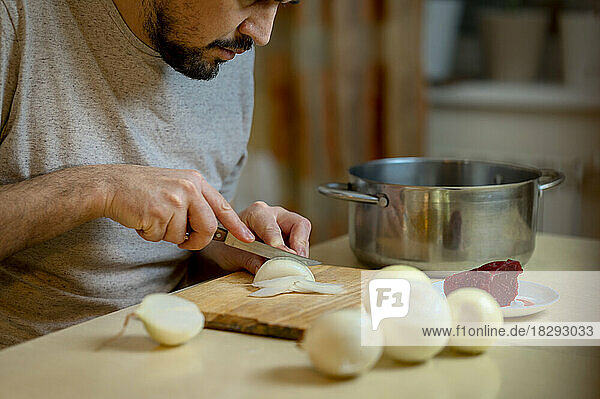 Man chopping white onion on cutting board in kitchen
