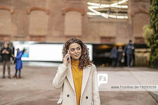 Smiling woman talking on smart phone standing in front of building