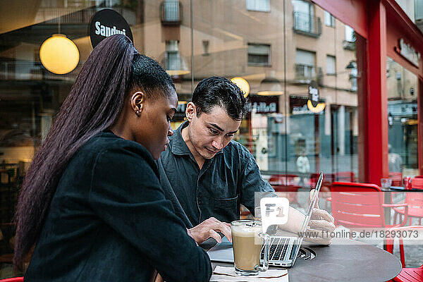 Multiracial colleagues working on laptop at sidewalk cafe