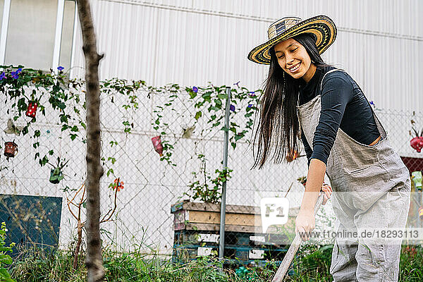 Happy woman gardening with rake in urban garden