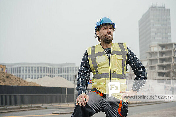 Contemplative mature blue-collar worker standing in front of construction site