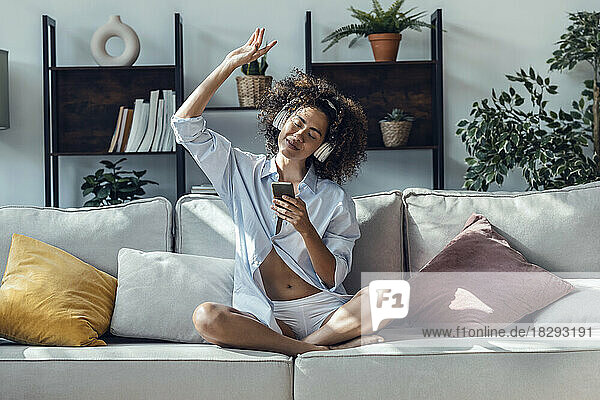 Young woman with mobile phone gesturing on sofa at home