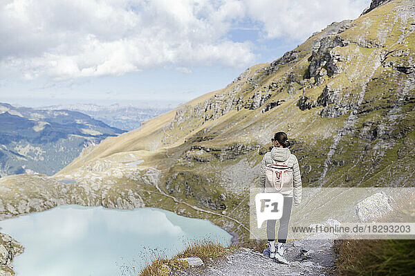 Wanderer mit Rucksack steht auf einem Felsen und blickt auf den Berg