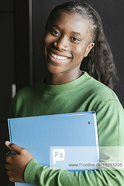 Smiling businesswoman holding file folder in front of wall