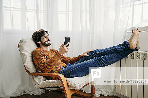 Happy man with smart phone sitting on armchair at home