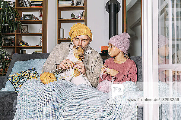 Father and daughter with dog knitting on couch at home together