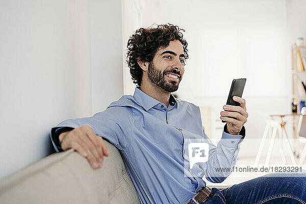Smiling businessman sitting with smart phone in office