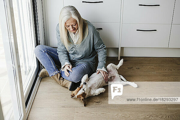 Mature woman stroking dog on floor at home