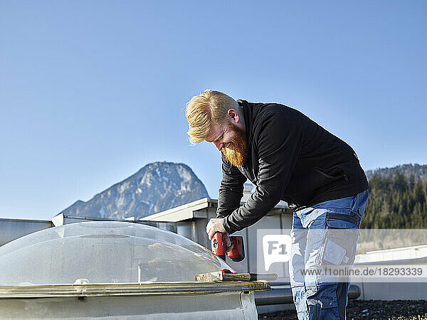 Roofer with work tool repairing roof on sunny day