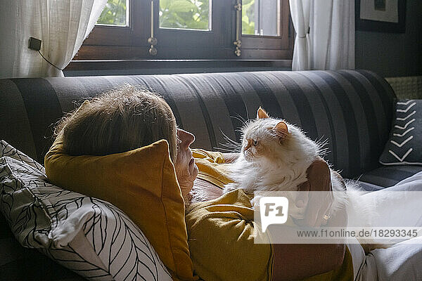 Ältere Frau kuschelt zu Hause mit Katze auf dem Sofa