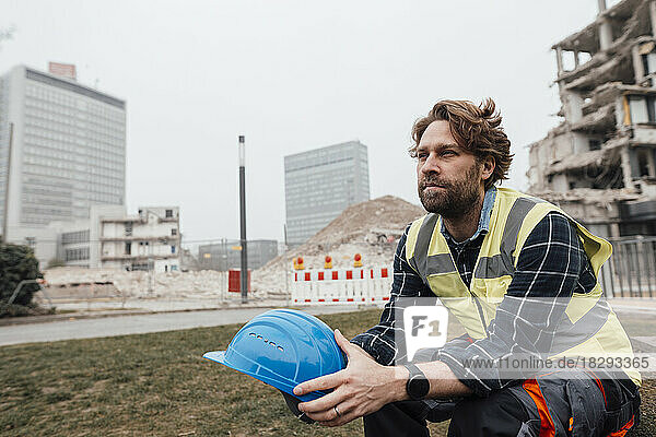 Contemplative mature worker sitting with hardhat at construction site