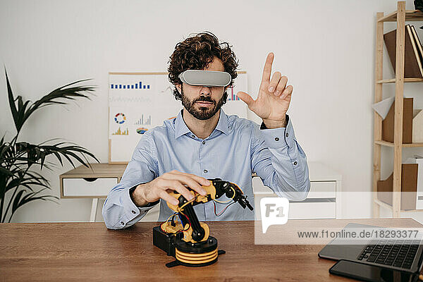 Businessman wearing virtual reality glasses with robotic arm on desk at office