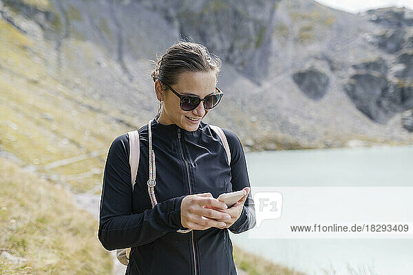 Smiling hiker using mobile phone near mountain lake