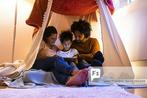 Mother and father using tablet PC with daughter sitting in tent at home
