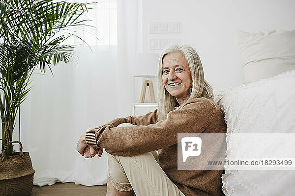 Happy mature woman sitting by bed in bedroom