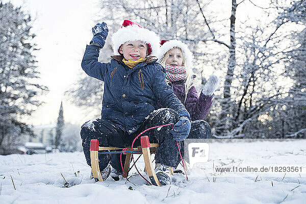 Cheerful brother with sister wearing Santa hats sitting on sled