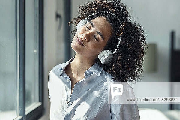 Woman with eyes closed listening to music through headphones at home