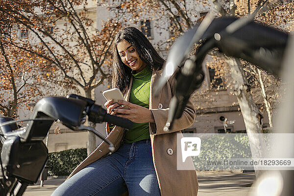 Glückliche junge Frau  die ihr Smartphone benutzt und auf dem Fahrrad sitzt