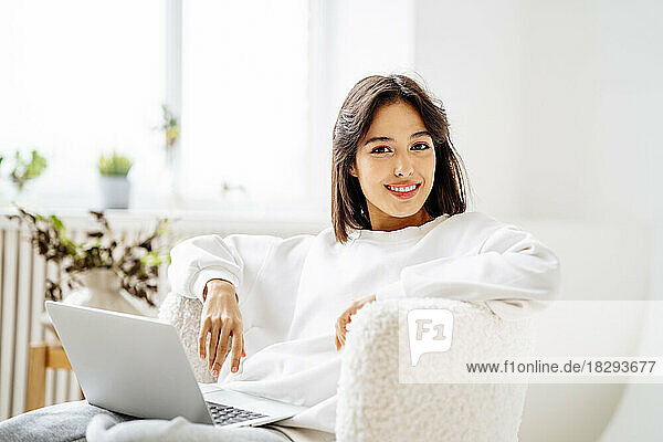 Happy woman resting on chair with laptop at home
