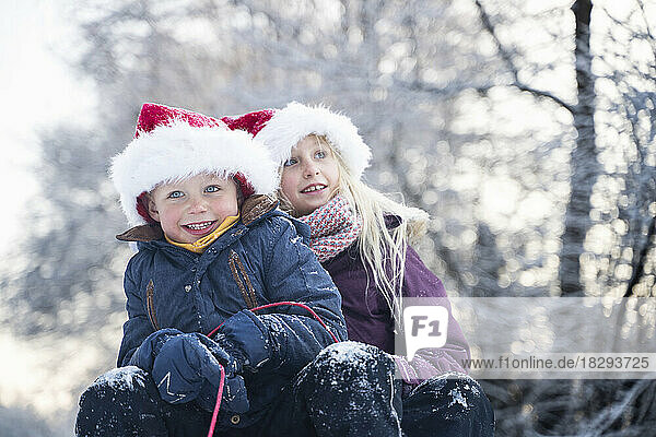 Happy brother and sister wearing Santa hats sitting on sled
