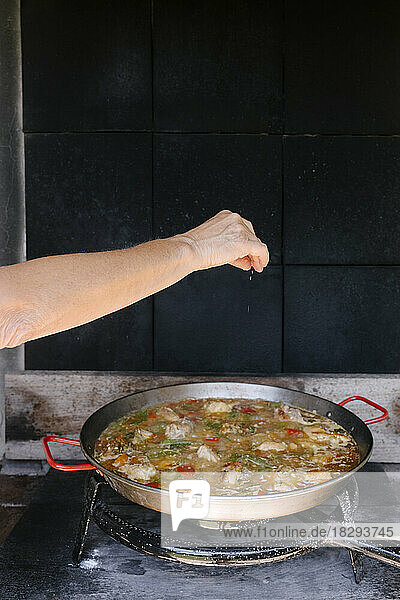 Woman sprinkling seasonings on paella at outdoor kitchen