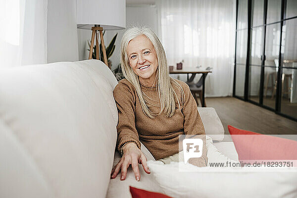 Happy mature woman sitting on sofa in living room