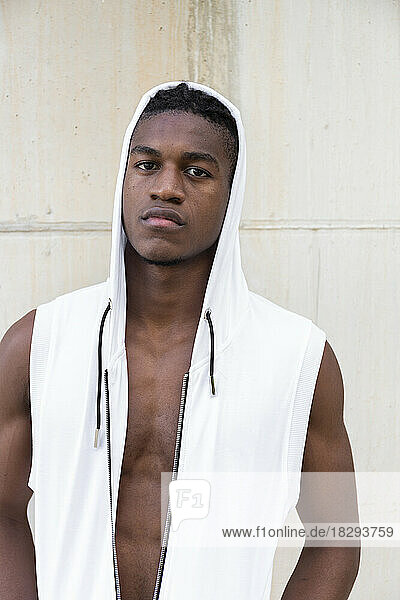 Serious young man wearing white hooded shirt in front of wall