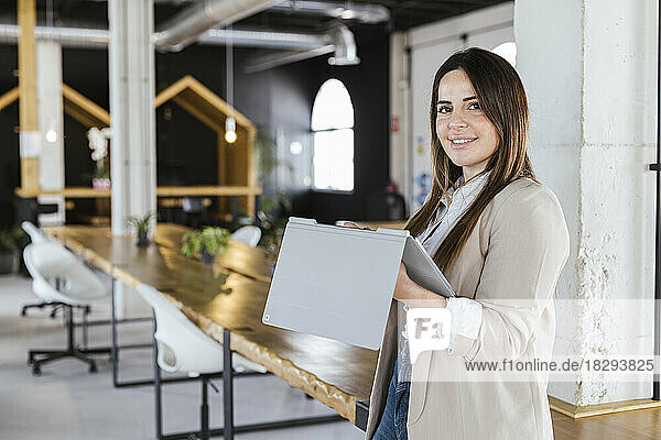 Smiling businesswoman with tablet PC standing in office