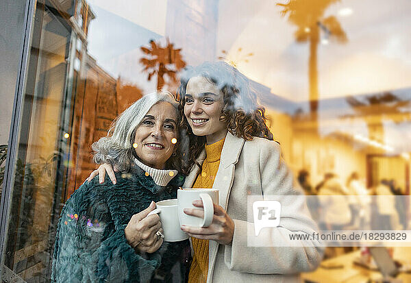 Happy young woman with grandmother holding coffee cup seen through glass
