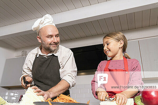 Father and daughter wearing aprons preparing healthy meal in kitchen at home