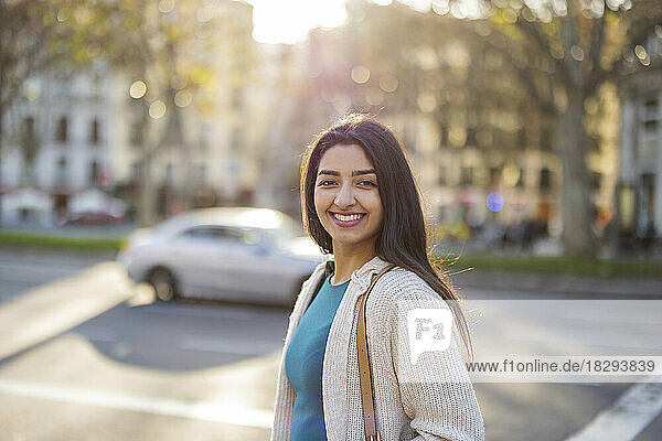 Smiling young woman standing at street on sunny day