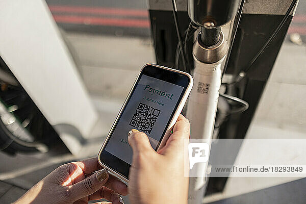 Young woman scanning QR code for renting bicycle