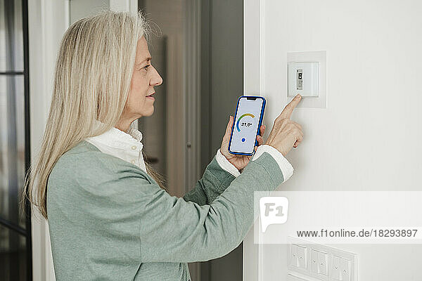 Reife Frau stellt zu Hause Thermostat mit Smartphone ein
